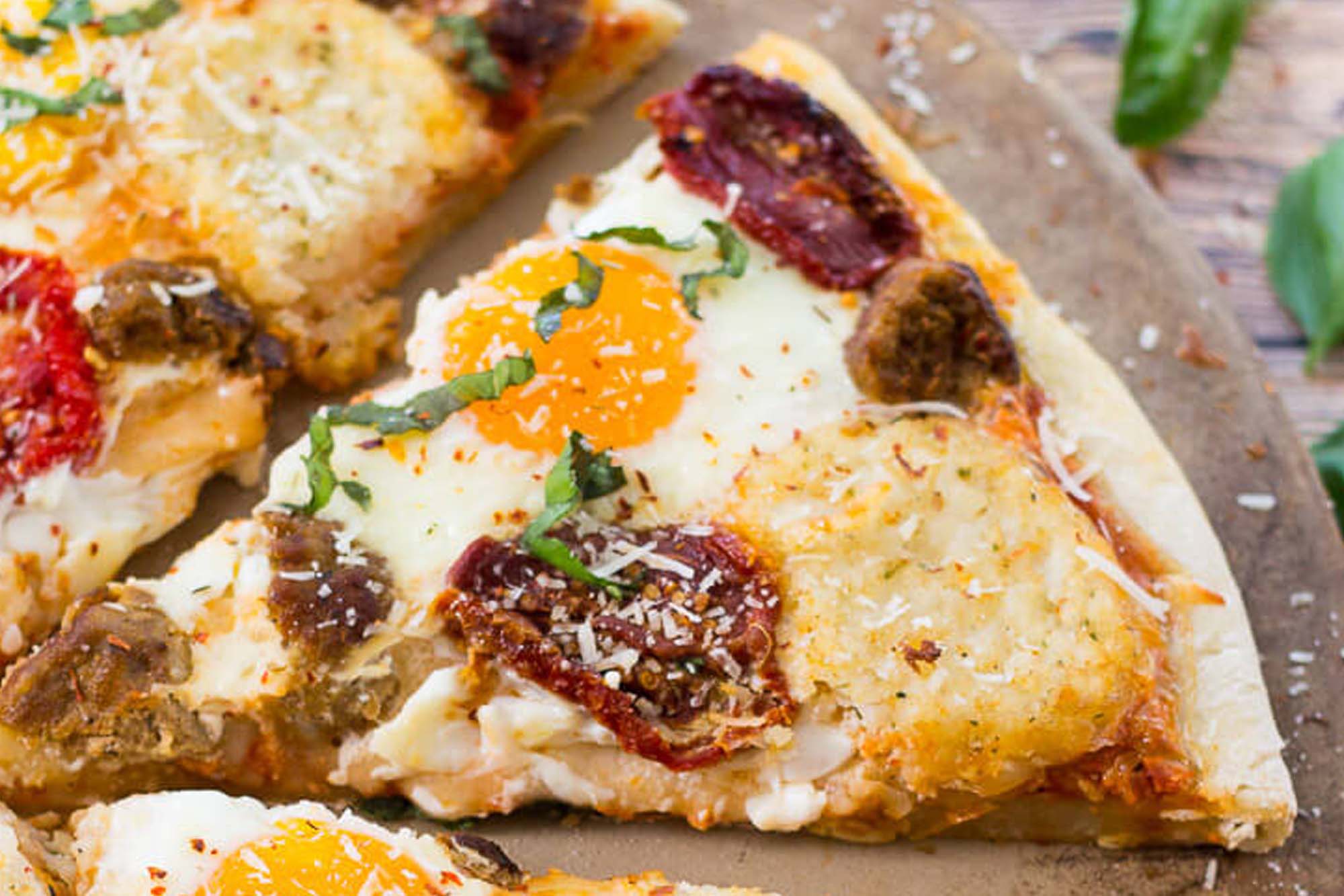 picture of a slice of breakfast pizza topped with egg, bacon, and sausage.